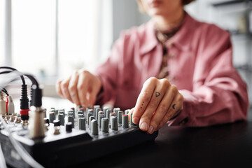 Close up of young female creator using audio mixer panel while setting up recording equipment in studio, copy space