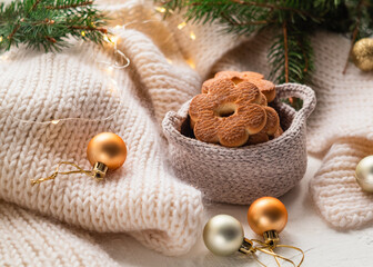 Christmas shortbread cookies on a white knitted blanket and Christmas balls. Flower shaped cookies in a crocheted light basket.