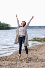 fashionable girl in trousers, blouse walks on the shore of the lake. sunset. girl jumping and having fun on the seashore