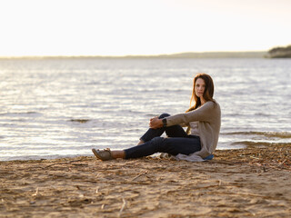 Fototapeta na wymiar fashionable girl in trousers, blouse walks on the shore of the lake. sunset. girl resting on the seashore