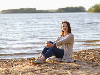 Fototapeta na wymiar fashionable girl in trousers, blouse walks on the shore of the lake. sunset. girl resting on the seashore