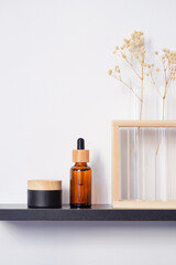 Amber glass dropper bottle and jar with bamboo lid on the black shelf. Skincare concept on white wall background. Spa natural cosmetic concept for face body care