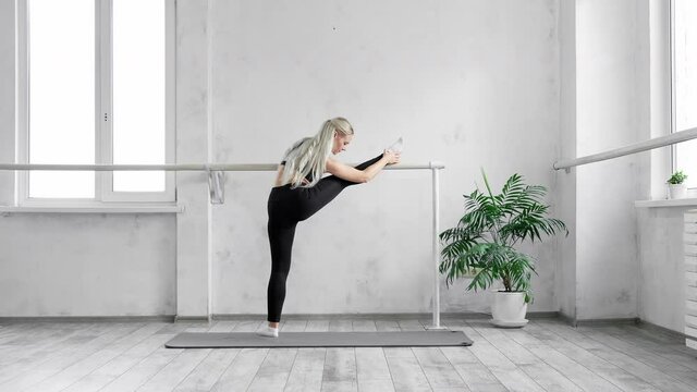 Young blonde woman doing stretching exercises using choreographic bar. Attractive fit woman stretching. Bodycare and fitness concept. 4K, UHD