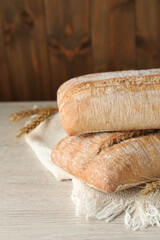 Fresh crispy ciabattas and spikelets on white wooden table, closeup