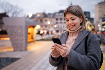 Beautiful charming girl in coat standing in street and looking at telephone.Nice winter day.