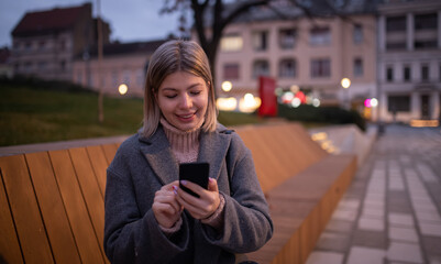Portrait of young woman using phone while waiting the bus outdoors.