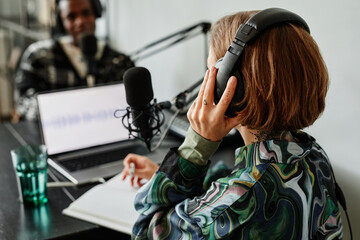 Back view of young woman recording podcast in studio and wearing headphones