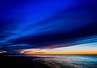 Dramatic blue cloudscape at dawn over the Atlantic Ocean. Analog-style saturated seascape at Falmouth Height Beach. Moody twilight hours on the empty beach at sunrise on Cape Cod in December.