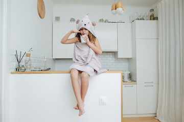 Focused little girl wrapped in a bear hooded towel, eating yogurt from a cup