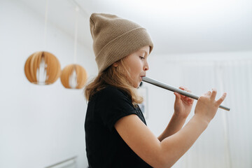 Side view of a little girl in a beige hat learning to play on an Irish flute