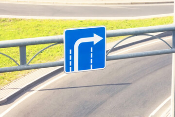 Blue road sign with an arrow turning from the outer lane on the background of a highway exit.