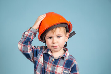 Serious little kid boy engineer or architect in a protective orange helmet