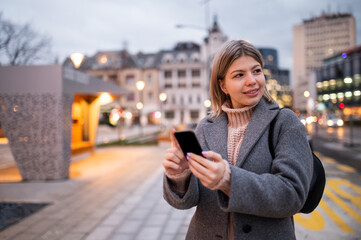 Beautiful charming girl in coat standing in street and looking at telephone.Nice winter day.