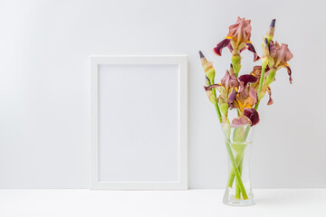 Home interior with decor elements. Mockup with a white frame and bouquet of irises flowers in a glass vase on a light background