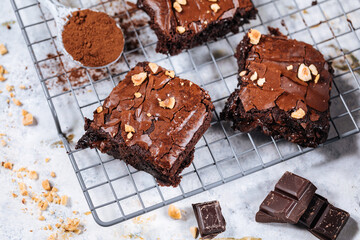 Chocolate brownies with hazelnut crumbs on top, on a tray with cacao powder, chocolate crumbs on a white rustic background. Very fudge brownies