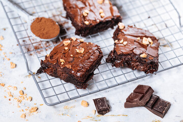 Chocolate brownies with hazelnut crumbs on top, on a tray with cacao powder, chocolate crumbs on a white rustic background. Very fudge brownies