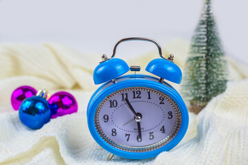 Alarm clock on the table with sweater in the background and decorations. Winter mood, festive decoration of a magical Christmas.