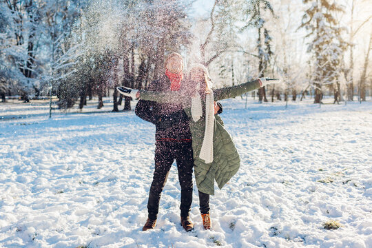 Happy young couple playing with snow in winter park. Man and woman having fun outdoors.