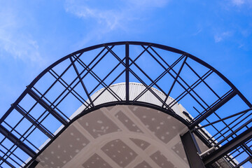 Fototapeta premium View from below of incomplete ceiling and curved metal awning structure in construction site against blue sky background