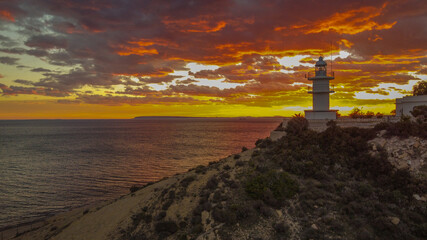 Faro mar&iacute;timo sobre atardecer rojizo con el mar en calma de poniente