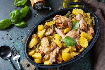 Baked chicken wings  with potatoes, beans, herbs, garlic  and bazil on pan, on dark stone tabletop. Home made food. Greek and Mediterranean Food.