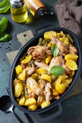 Baked chicken wings  with potatoes, beans, herbs, garlic  and bazil on pan, on dark stone tabletop. Home made food. Greek and Mediterranean Food.