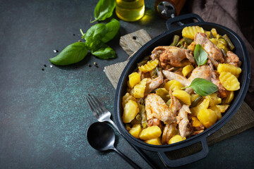 Baked chicken wings  with potatoes, beans, herbs, garlic  and bazil on pan, on dark stone tabletop. Home made food. Greek and Mediterranean Food. Copy space.
