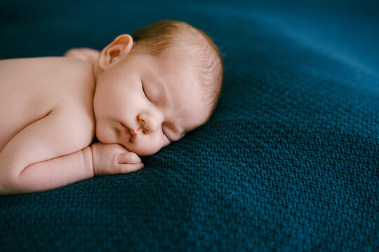 Naked baby sleeping on a blue blanket with his hand under his cheek