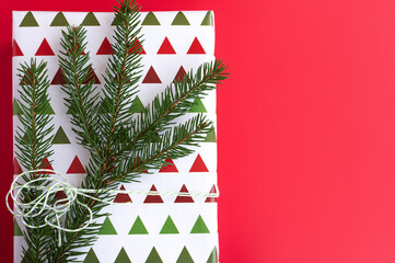 gift in beautiful package with a coniferous twig on a red background. Flat lay, copy space 