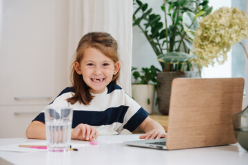 Showing missing teeth little girl sitting behing a big table, drawing