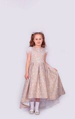 A happy little school-age girl in a long chic expensive dress, isolated on a white background. Full-length photo