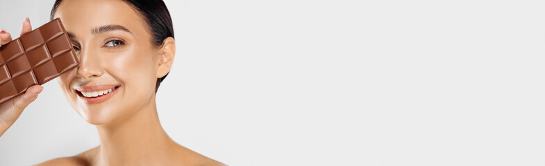 beautiful woman with makeup holding a chocolate bar on her face, isolated on white background. Spa...