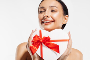Portrait of a delighted young woman holding a heart-shaped red gift box on a white background