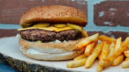 cheeseburger  with cheddar chese, russian salad, pickled cucumbers, french fries on wooden tray with brick wall background