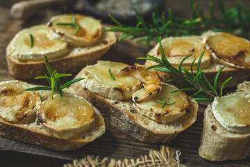 Baguette bread slices baked with goat cheese and honey, decorated with rosemary, on wooden...