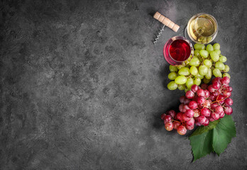 Red and white wine in wineglasses and grape on dark stone background. Top view