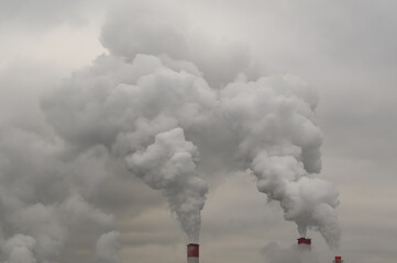 exhaust from industrial pipes from a production or thermal power plant. Steam or polluted smoke escapes from the pipes into the gray cloudy sky