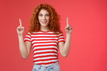 Excited good-looking cheeky redhead ginger girl curly natural hair pointing raised index fingers up...