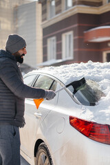 A young man cleans his car after a snowfall on a sunny, frosty day.