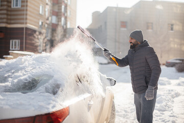 A young man cleans his car after a snowfall on a sunny, frosty day.