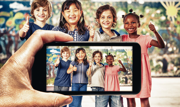 Male hand with smartphone taking a picture of children group smiling at school