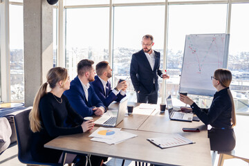 The boss stands near the board with graphs, demonstrates statistics, various personnel attending the training, introduces the new products of the company, reports on the results of work for partners.