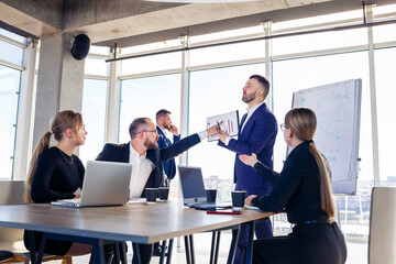 Confident businessman makes a presentation of a new project in the boardroom at a company meeting. Beautiful auditors talk with different partners about the business using a whiteboard and graphs.