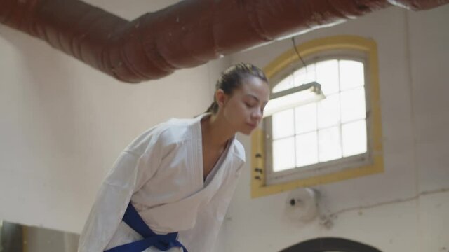 Slider shot of girl bowing before starting karate workout. Front view of confident and serious Caucasian female fighter performing greeting, getting ready for practice. martial arts, sport concept