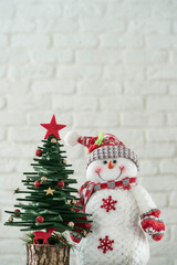 Christmas background with pine tree and Snowman ornaments over brick wall surface with copy space.