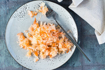 Fresh sauerkraut with carrots and a fork on a plate on the table. Fermentation and a vegetarian diet. Top view. Close-up