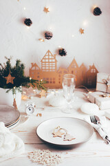Organization of a festive Christmas table. Plate, cutlery, champagne glass and Christmas decorations. Tablescapes  on white wooden table. Vertical view