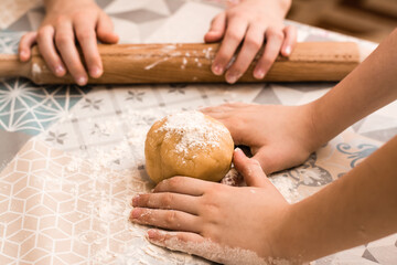 Children's hands prepare to use a rolling pin to roll ginger dough to bake Linzer cookies on the table in the kitchen. Lifestyle