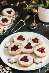 Ready Linzer cookies with berry jam on a plate and Christmas decorations on a dark background. Cooking Christmas treats. Lifestyle. Vertical view. Close-up