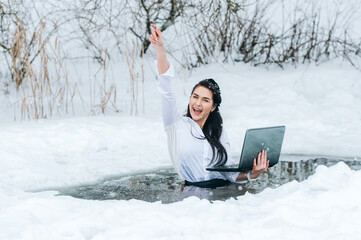 Girl with laptop in frozen lake ice hole. Woman hardening the body in cold water. Good immunity is...